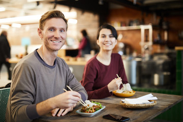 Portrait of happy young couple looking at camera while enjoying Asian food in restaurant, copy space