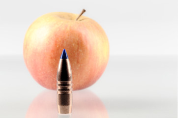 Copper bullet and an apple on a gray background, a bullet in front of an apple, shallow depth of...