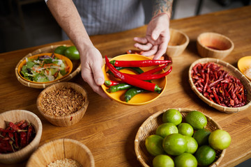 Close up of professional chef holding chili peppers and spices while cooking in restaurant kitchen,...