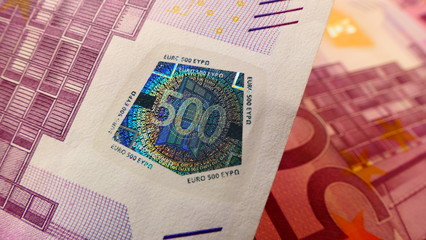 Close-up view of a 500 Euro banknote with security seal and multiple 500 Euro banknotes in the background