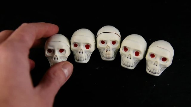 human hand take away one by one white chocolate candy in skeleton skull shape with red eyes served on black background