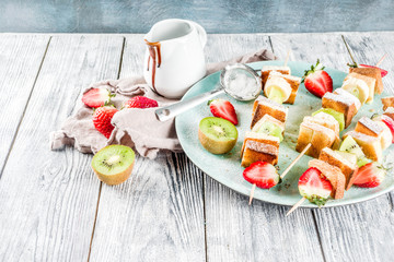 Summer breakfast snack. Fruit vegan dessert kebabs on skewers with toast French fried bread, fruits and berries. With powdered sugar and chocolate sauce.
