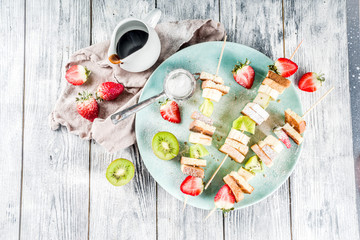 Summer breakfast snack. Fruit vegan dessert kebabs on skewers with toast French fried bread, fruits and berries. With powdered sugar and chocolate sauce.