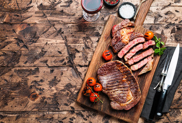 Sliced grilled Medium rare beef steak Ribeye with seasonings and red wine on wooden cutting board, top view