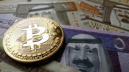 Bitcoin, an virtual currency in physical coin form, displayed on Saudi Arabian Riyal banknotes