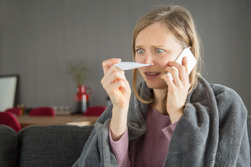 Worried woman checking temperature and calling doctor on phone