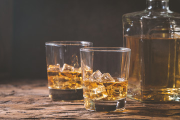Whiskey with ice in glasses on rustic wood background, copy space
