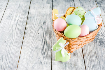 Easter greeting card background with pastel colored eggs and homemade cookies shaped in eggs and bunnies rabbits. With a basket, tulips, rustic wooden table, copy space top view banner
