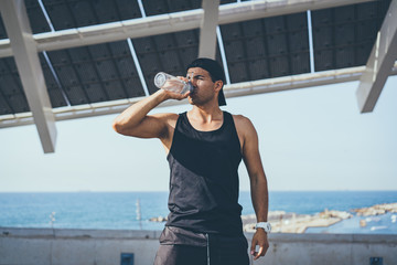 Fototapeta premium Muscular Male athlete sprinter drinking pure water after hard workout exercise. Healthy lifestyle