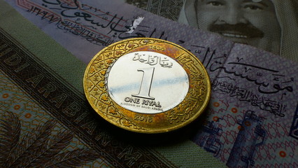 Close-up view from the frontside of one Saudi Riyal coin with multiple Riyal banknotes in the background