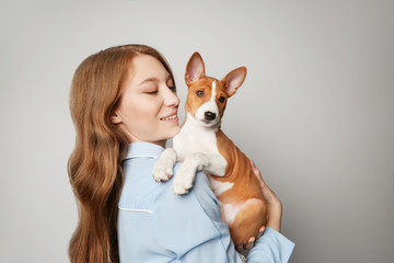 Beautiful red haired girl embracing puppy on white background. Studio portrait of white appealing woman chilling with dog.
