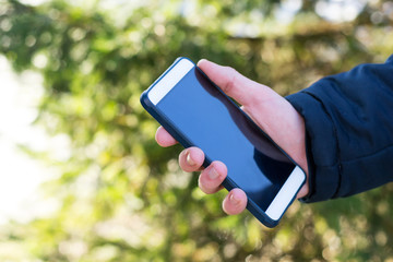Closeup male hand holding mobile phone outdoors in sunny day. Copy space, communication, business, work, texting concept