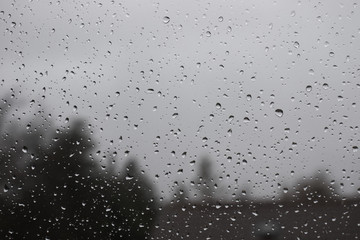 Water drops on window with blurred trees and house in background.