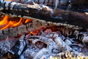Glowing embers in the ash with log in smoke, macro