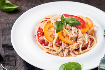 spaghetti with tuna, tomatoes and garlic sauce on white plate over dark background