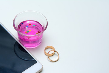 Near the white smartphone - a wedding candle and wedding rings. Concept - wedding anniversary