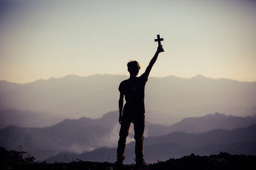 Silhouette of human hand holding cross, the background is the sunrise., Concept for Christian,...