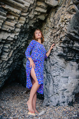 A young girl in a blue dress with polka dots hid in a cave, walking on the coast of the ocean. The concept of rest on the rocky coast.
