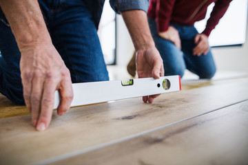 A midsection of man with his father laying vinyl flooring, a new home concept.