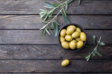 Fresh green olives in a bowl and olive branch on rustic wooden background, top view