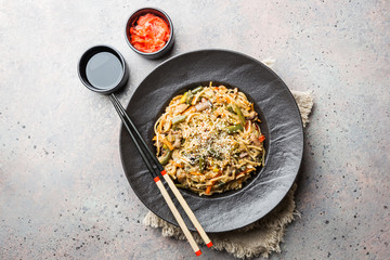 Plate of wok or stir fry noodles with meat and vegetables over gray stone background, top view