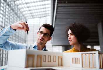 Young architects with model of a house standing in office, talking.
