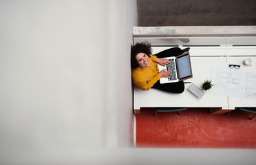 A top view of young businesswoman sitting on desk in an office, using laptop.