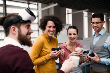 A group of young businesspeople with VR goggles in office, talking.