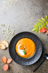 Pumpkin soup in a black plate on a stone background. Autumn decorations. Top view