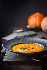 Pumpkin soup in a black plate on dark wooden background. Autumn decorations.