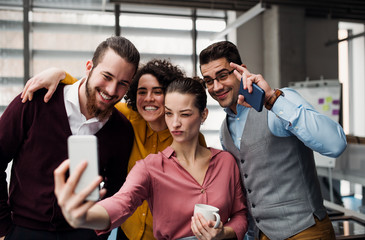 A group of young businesspeople with smartphone in office, taking selfie.