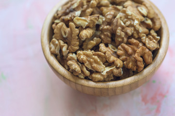 Walnuts kernels, peeled nuts in a wooden bowl on a pink background