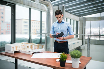 Young businessman or architect with model of a house standing in office, working.