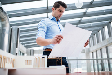 Young businessman or architect with model of a house standing in office, working.