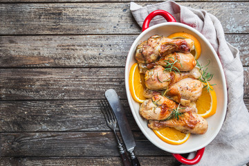 Baked chicken drumstick in a dish with orange and rosemary, top view