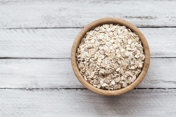 Uncooked oatmeal or oat flakes in a wooden bowl on a white wooden background