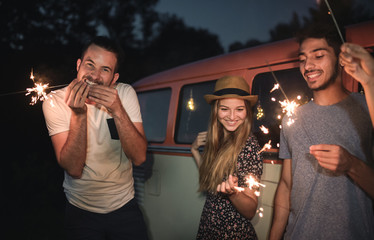 A group of friends with sparklers standing outdoors at dusk.