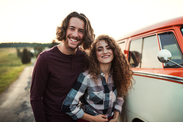 A young couple on a roadtrip through countryside, standing by minivan.