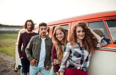 A group of young friends on a roadtrip through countryside, standing by a minivan.