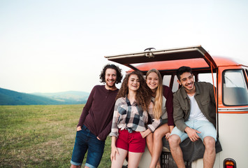 A group of young friends on a roadtrip through countryside, standing by a minivan.