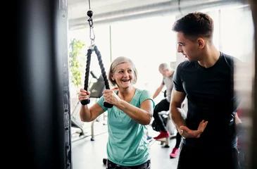  A female senior with a young trainer doing strength workout exercise in gym. © Halfpoint