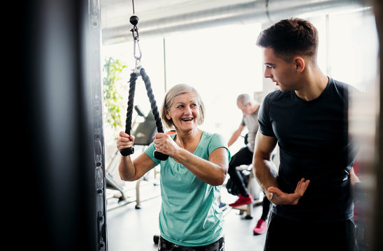 A Female Senior With A Young Trainer Doing Strength Workout Exercise In Gym.