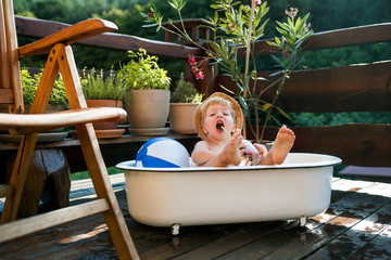 Small boy with a hat in bath outdoors in garden in summer, playing in water.