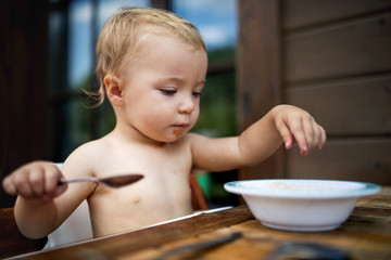 Small girl standing by a table on a patio in summer, eating soup.