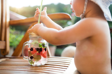 A midsection of small girl with a drink standing by a table on a patio in summer.