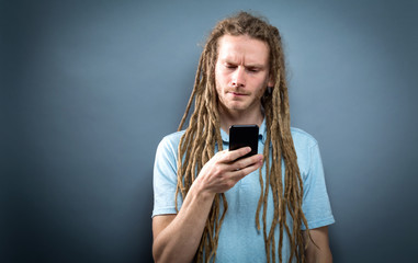 Young man staring at his cellphone on a gray background