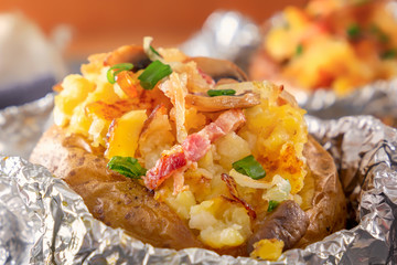 Baked potato in foil with bacon, onions and mushrooms on a gray wooden table. Close-up