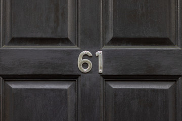 House number 61 in silver numbers on a black wooden door - sixty one is screwed onto the door