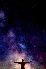 dark silhouette of man with opened hands under beautiful bright night sky with Milky way. Space...
