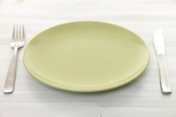 empty green dish on the white wooden table with fork and knife